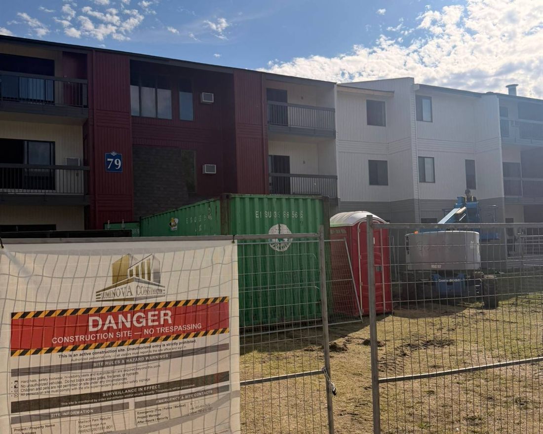 A three-storey apartment complex under renovation by Luminova Construction, with site hoarding, storage containers and a boom lift in the compound